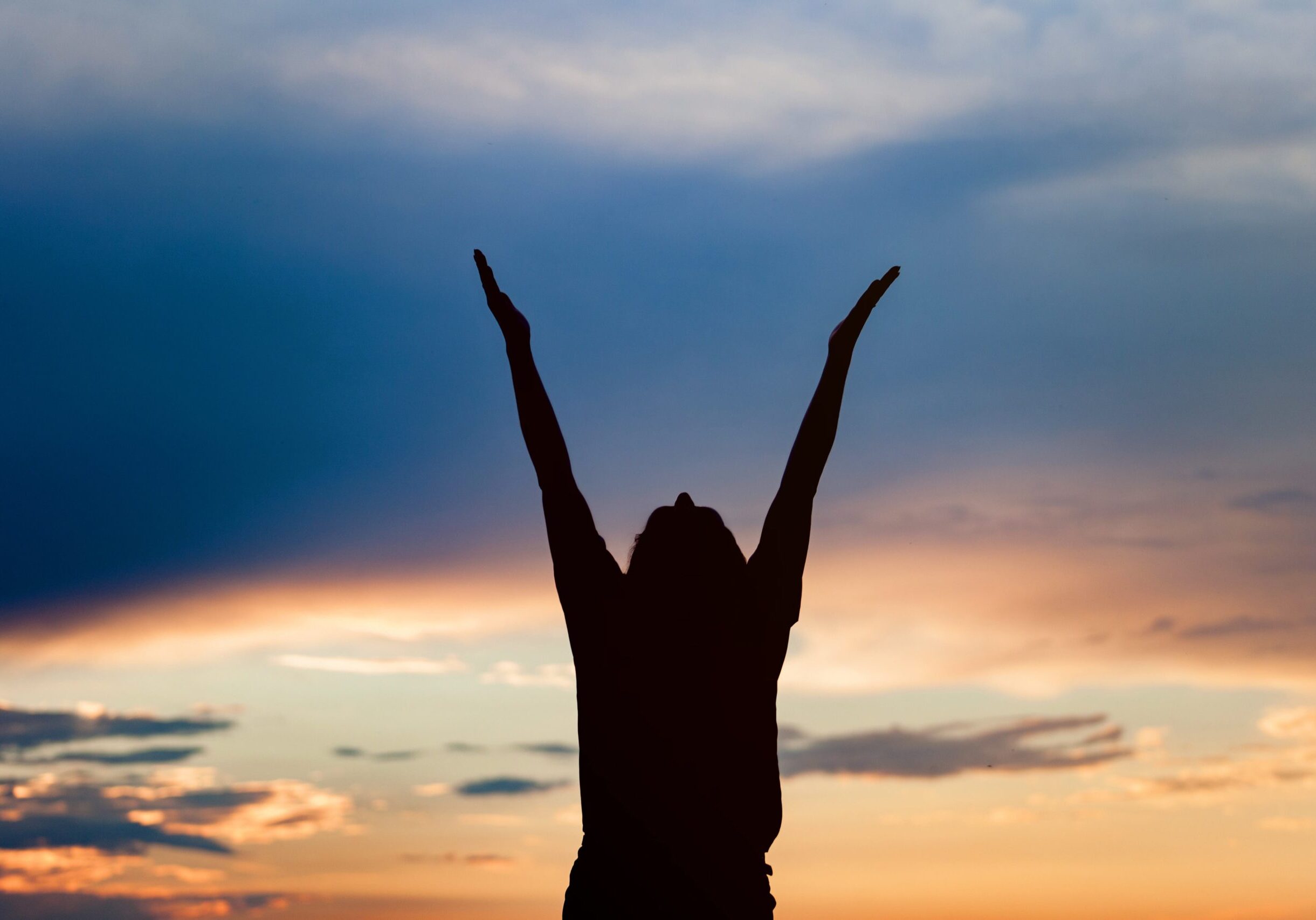 Happy celebrating winning success woman at sunset or sunrise standing elated with arms raised up above her head in celebration of having reached mountain top summit goal during hiking travel trek.